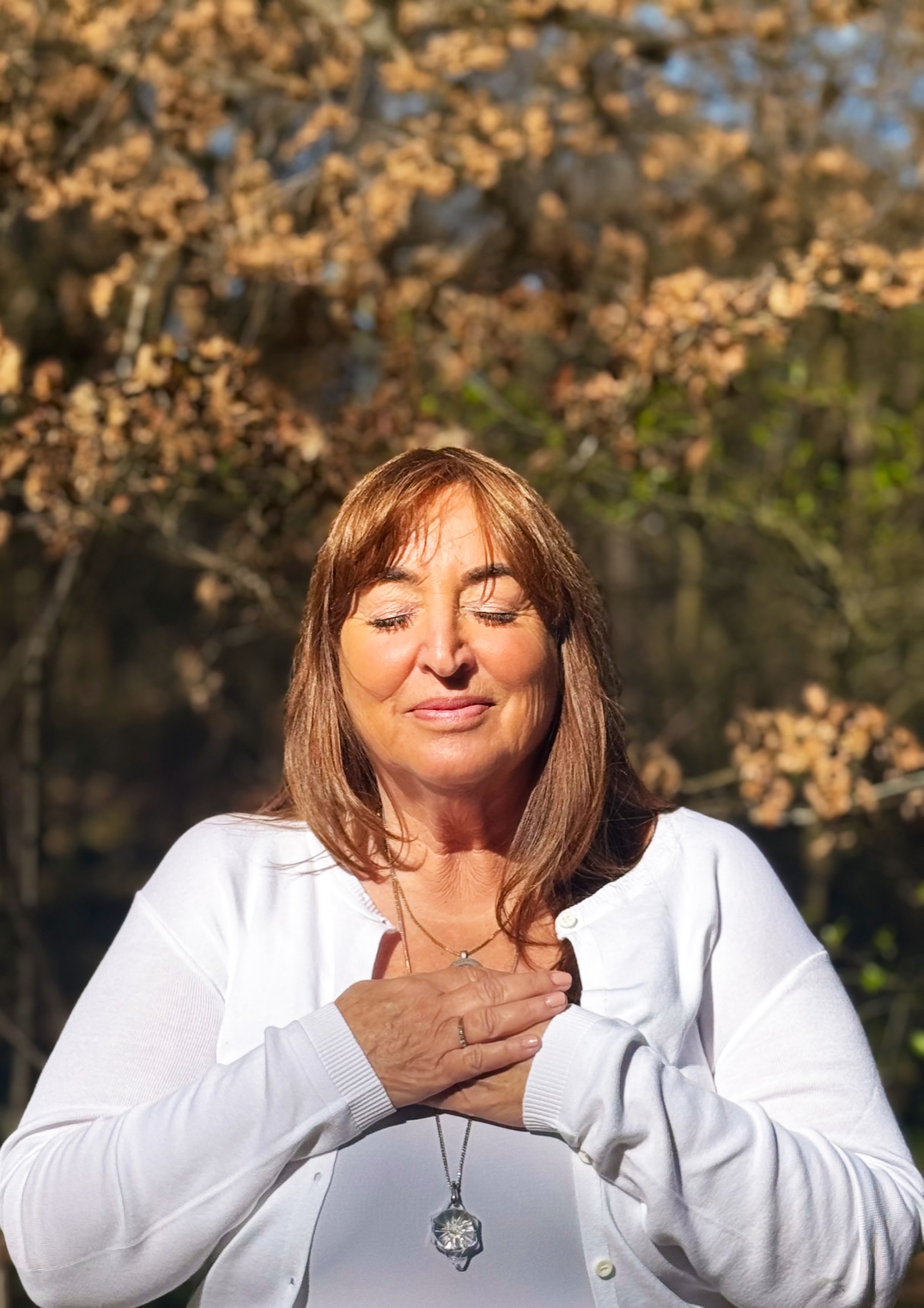 Margaretha in een witte trui buiten in de zon, met gesloten ogen en haar handen op haar hart