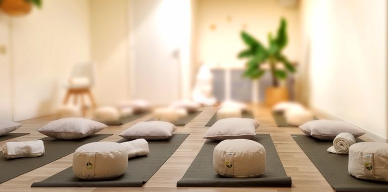 Lichte ruimte met yogamatjes, meditatiekussens en opgerolde dekens klaargelegd voor het weekend